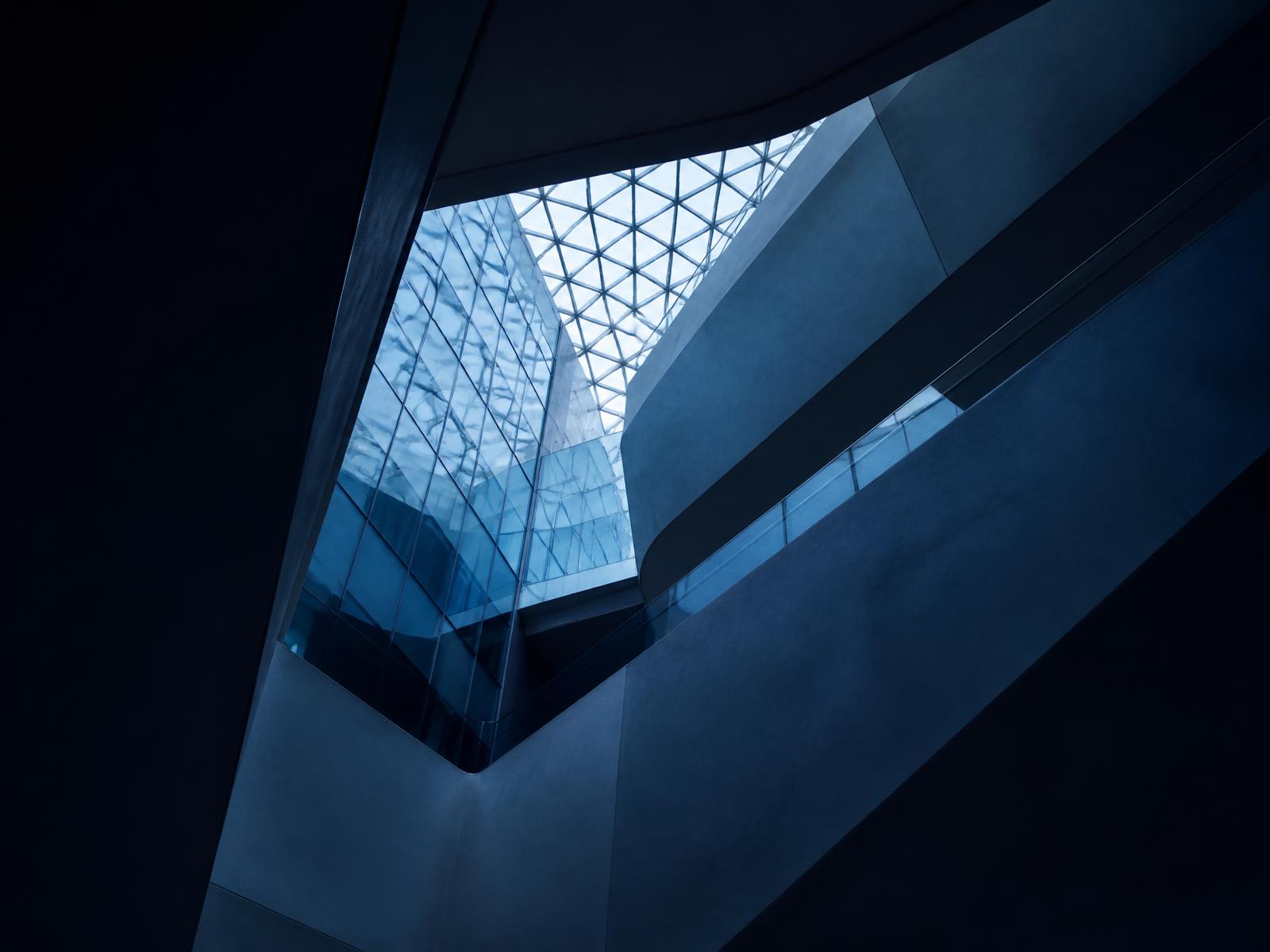 Abstract view of a modern glass atrium in deep navy and teal light.