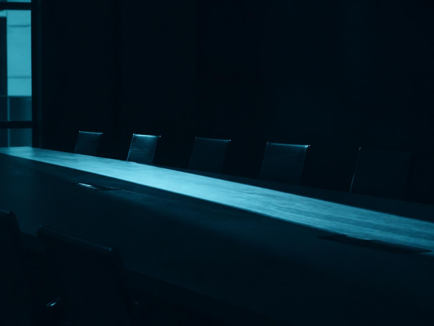 Abstract view of an empty boardroom table lit by a single band of daylight.